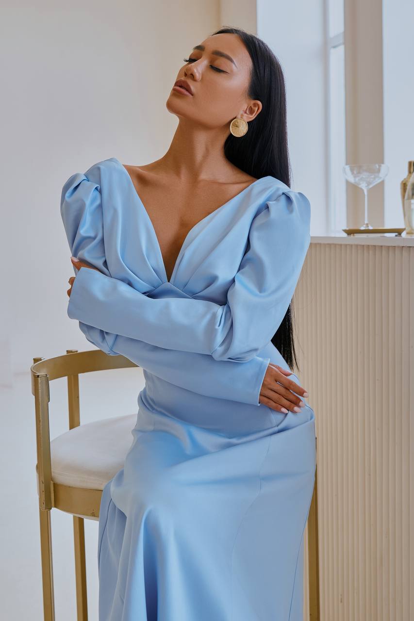 Woman in a light blue dress sitting on a chair indoors.