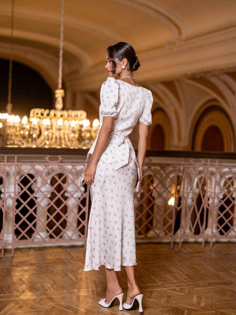 Woman in a white dress standing in an elegant indoor setting with chandeliers.