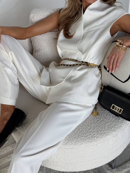 Person wearing a white outfit with a gold chain, sitting on a textured surface.