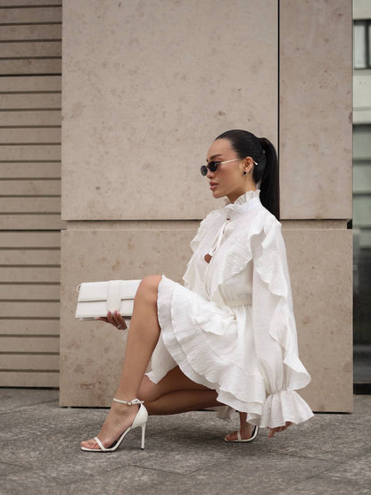 Woman in a white dress sitting against a beige wall.