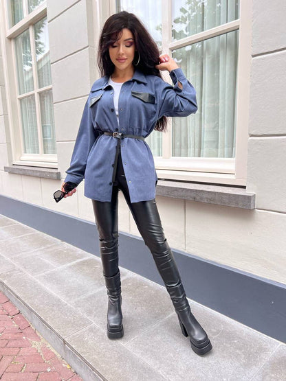 Woman in a blue trench coat and black leather pants standing on a sidewalk.