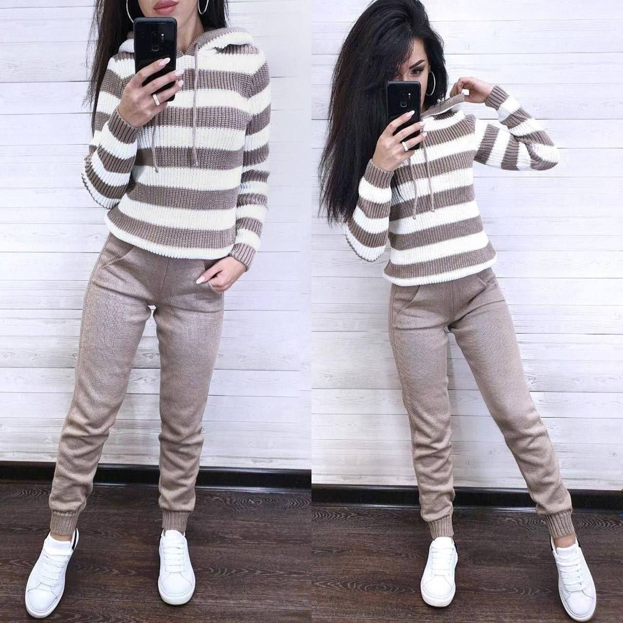 Woman wearing a striped sweater and beige pants, standing in front of a mirror.