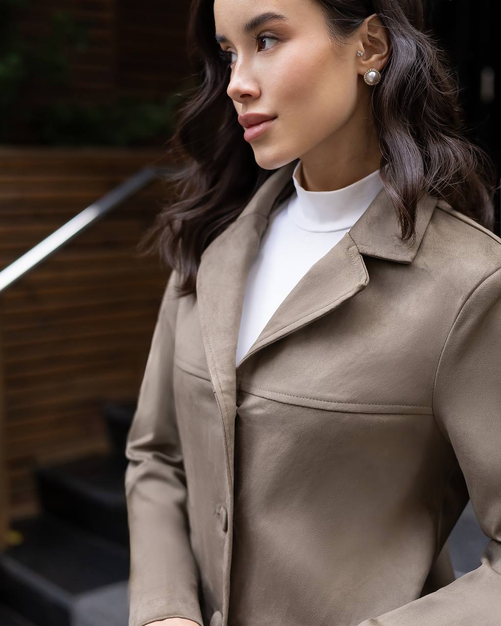 Woman wearing a beige coat over a white turtleneck, standing outdoors.
