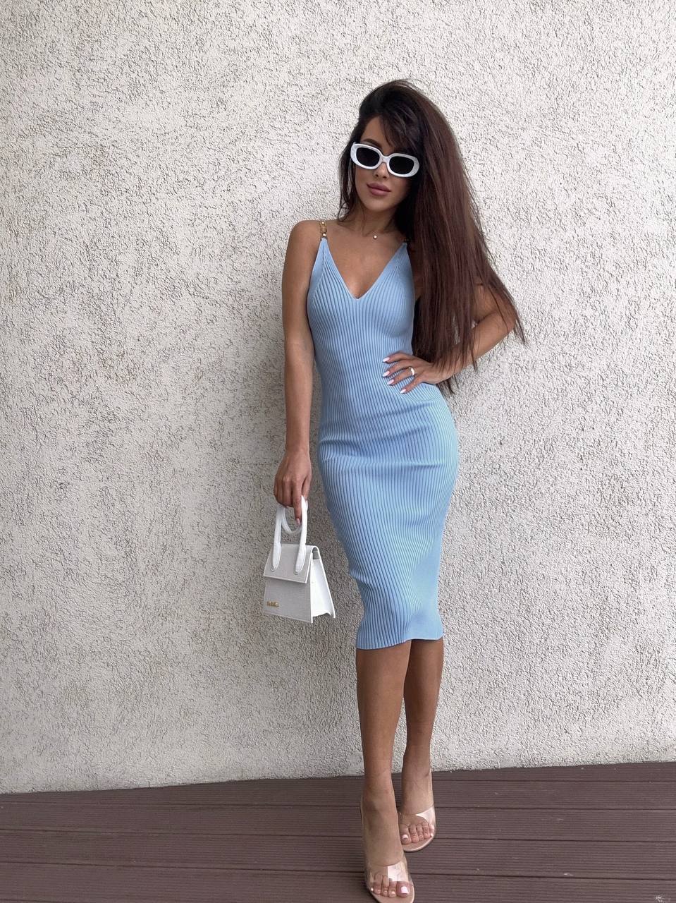 Woman in a light blue dress standing against a textured wall.