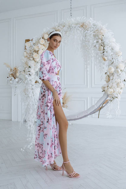 Woman in a floral dress standing in front of a decorative floral wreath in a white room.