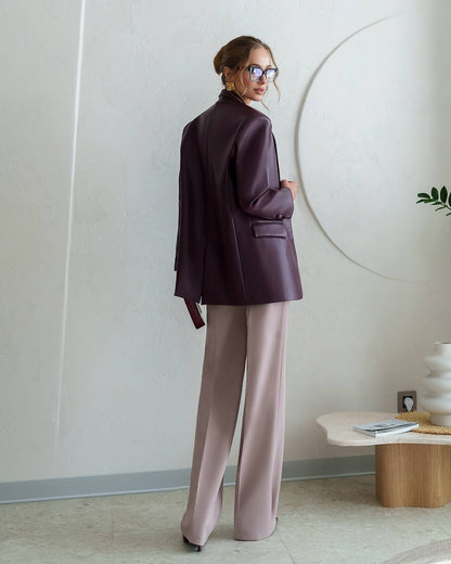 Woman in a dark purple blazer and light pink pants standing in a minimalistic room.