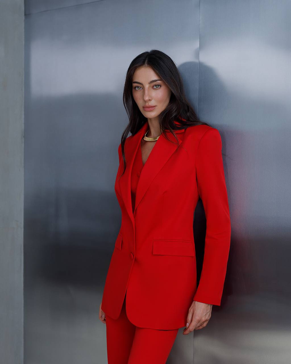 Woman in a red suit standing against a gray wall
