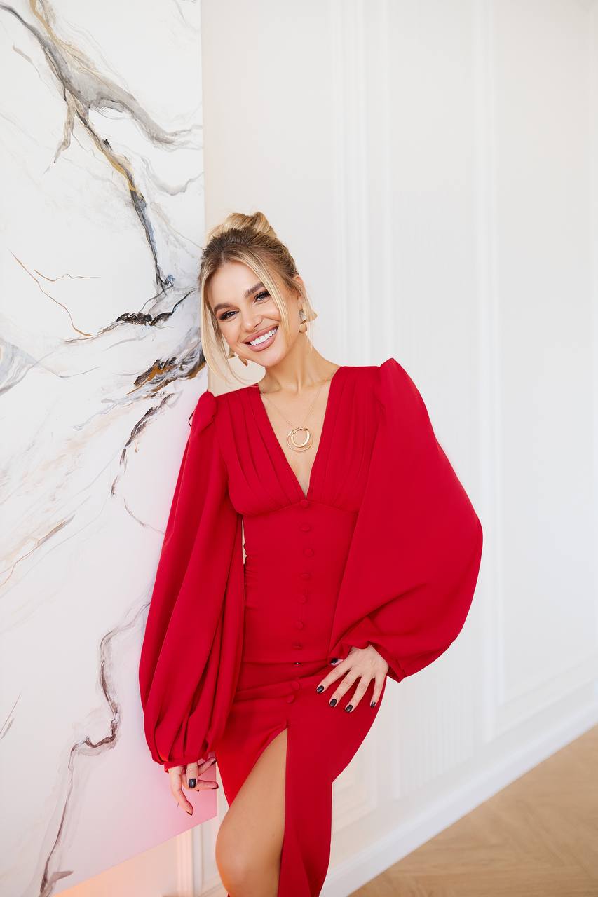 Woman wearing a red dress with long sleeves against a marble wall.