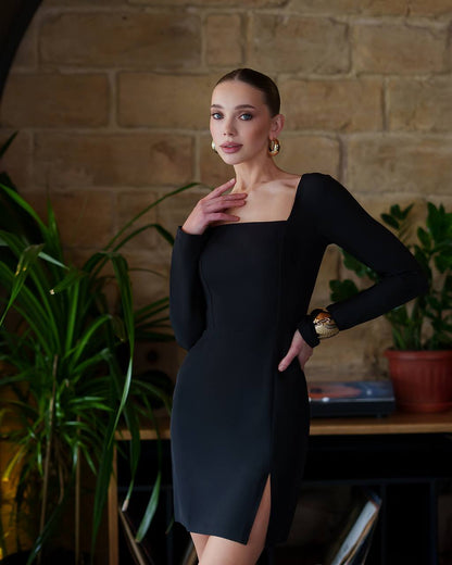 Woman in a black dress posing against a brick wall with plants.