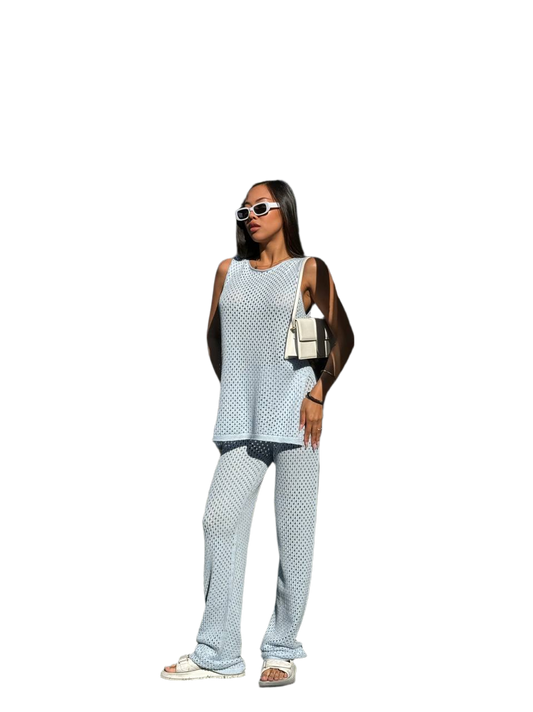 Woman wearing a light blue sleeveless top and pants with sunglasses and a handbag on a white background
