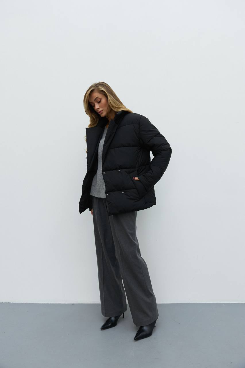Person wearing a black puffer jacket and gray pants against a white background