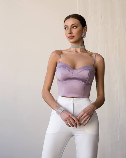 Woman wearing a lavender top and white pants against a neutral background