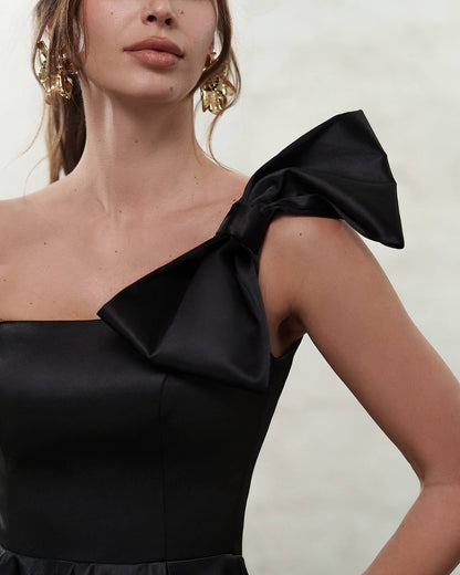 Black one-shoulder dress with a large bow detail on a neutral background