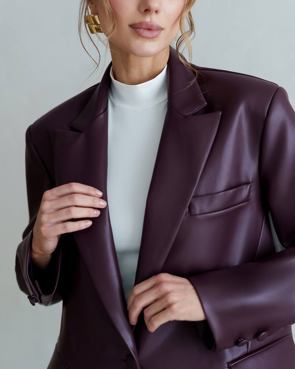Person wearing a dark purple blazer over a white shirt against a neutral background