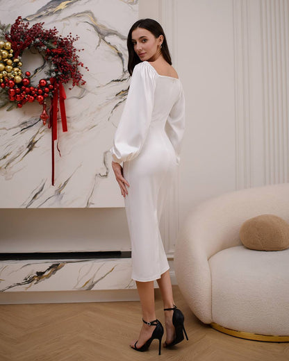 Woman in a white off-shoulder dress standing in a stylish room with decorative wreath.