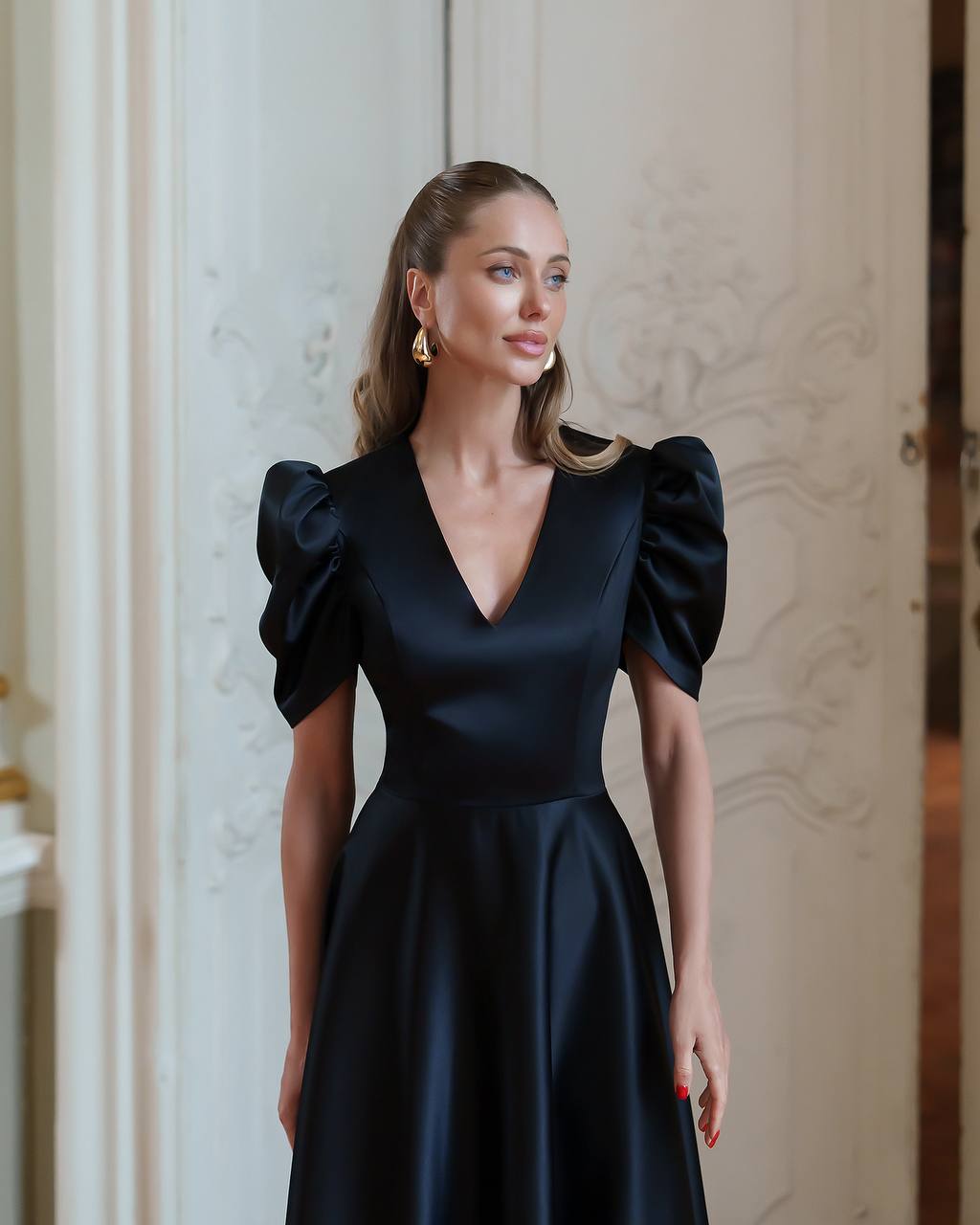 Woman wearing a black dress with puffed sleeves in an elegant interior setting