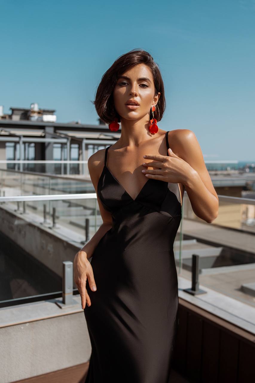Woman in a black dress with red earrings on a rooftop with a cityscape background