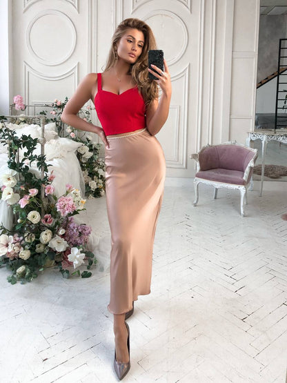 Woman taking a mirror selfie wearing a red top and beige skirt in a decorated room.