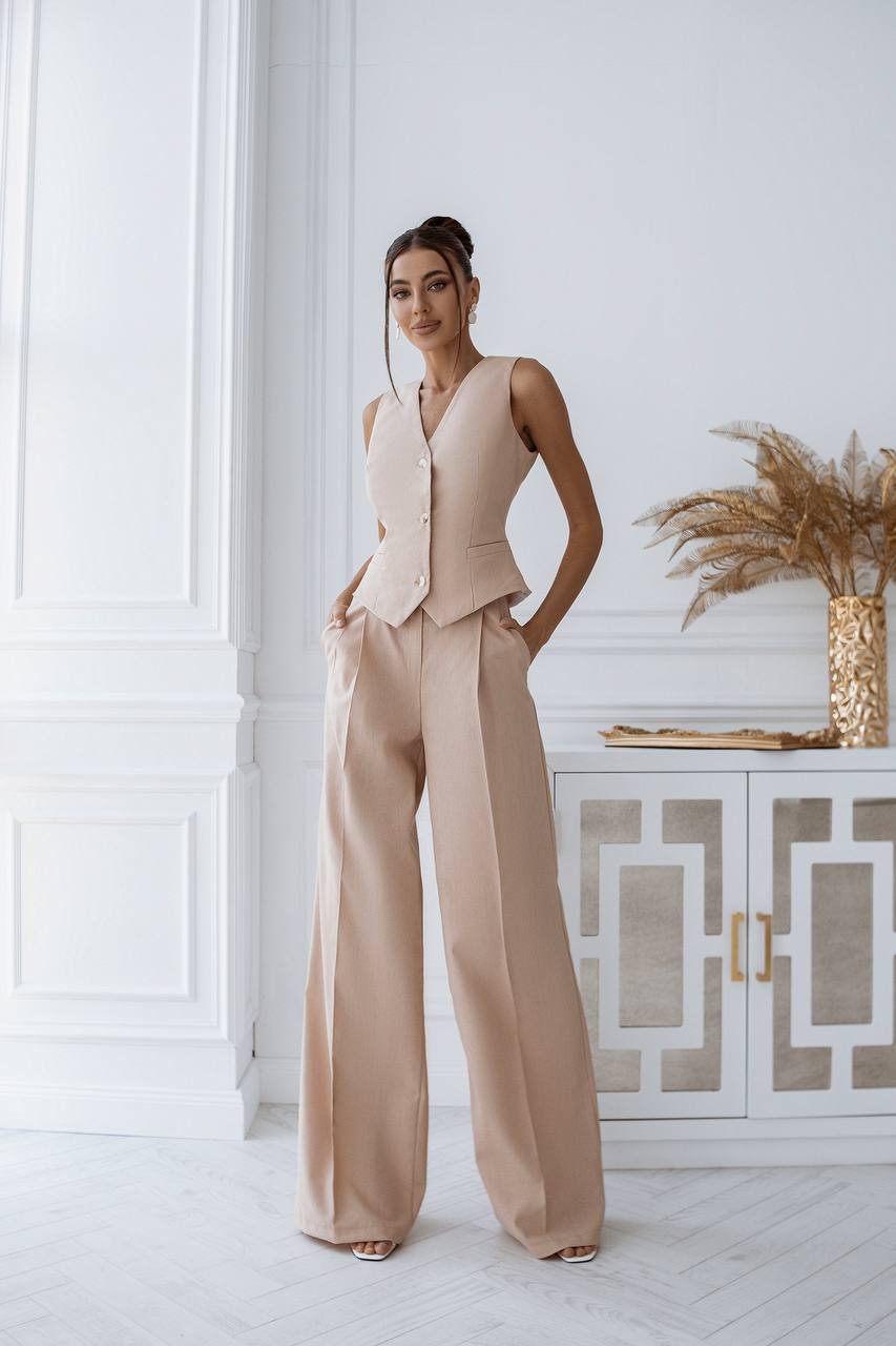 Woman in a beige outfit standing in a stylish interior setting.
