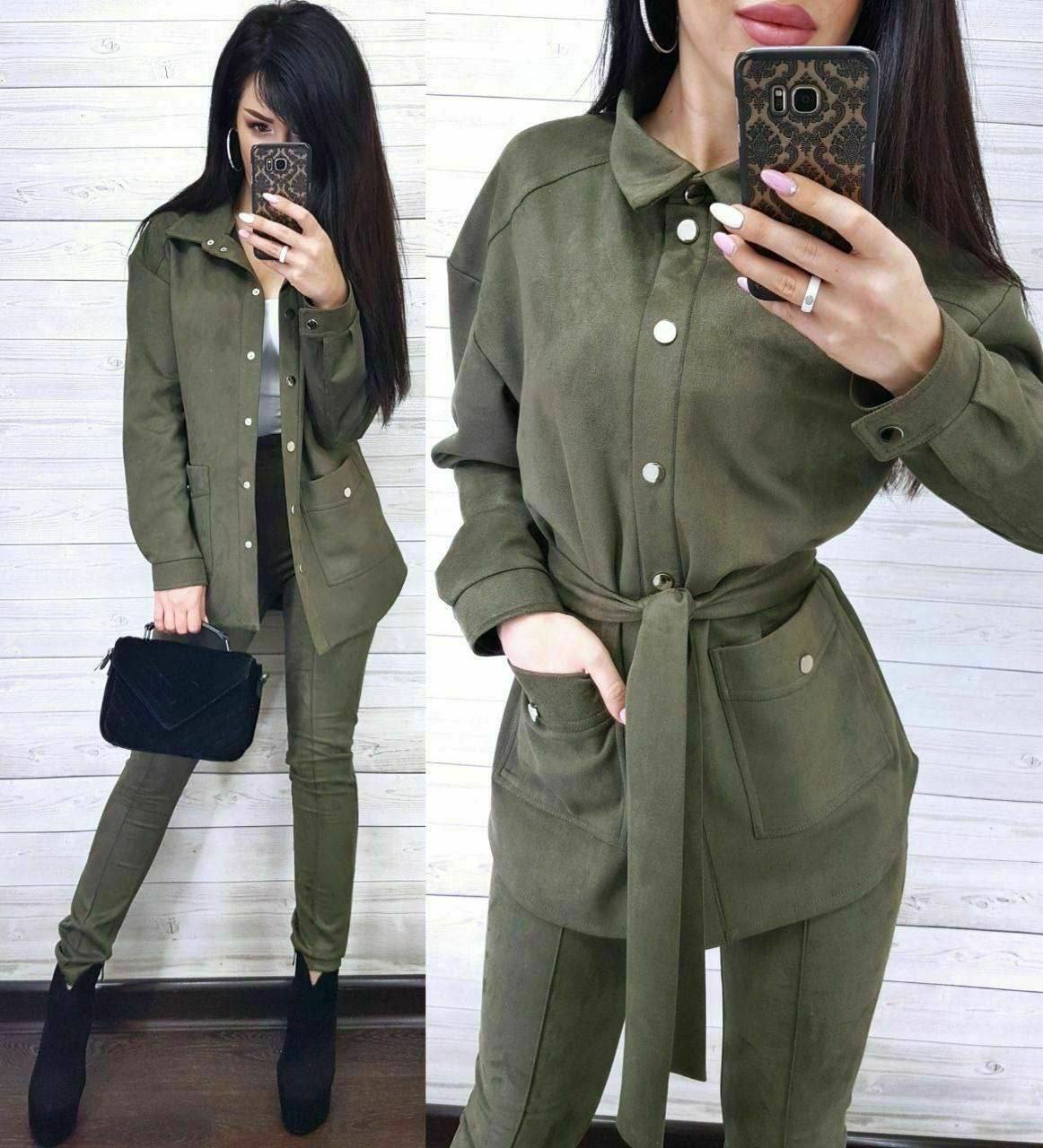 Woman wearing an olive green outfit with a belt, taking a mirror selfie.