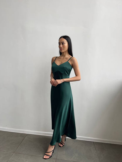 Woman wearing a green dress standing against a plain white wall.