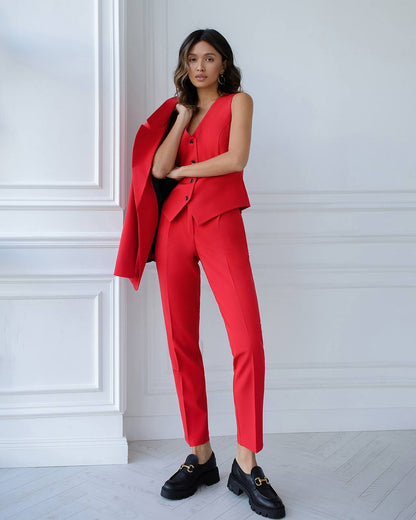 Woman wearing a red suit with black shoes against a white paneled wall.