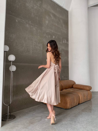 Woman in a beige dress standing in a modern living room with a brown sofa and white walls.