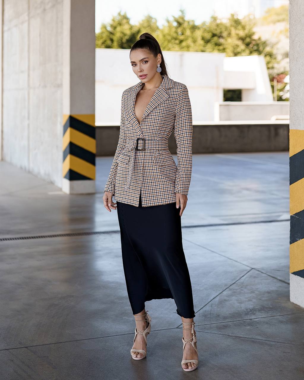 Woman in a checkered blazer and black skirt standing in an outdoor setting.