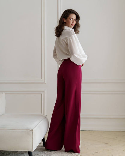 Woman wearing a white blouse and burgundy pants in an elegant room.