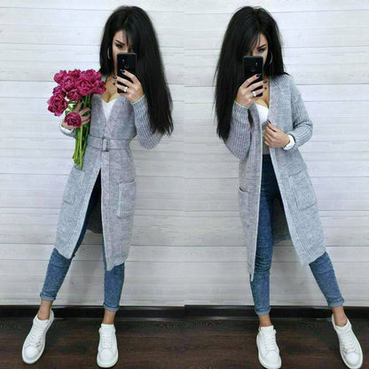 Woman wearing a long gray cardigan over a white shirt, blue jeans, and white sneakers, holding pink flowers.