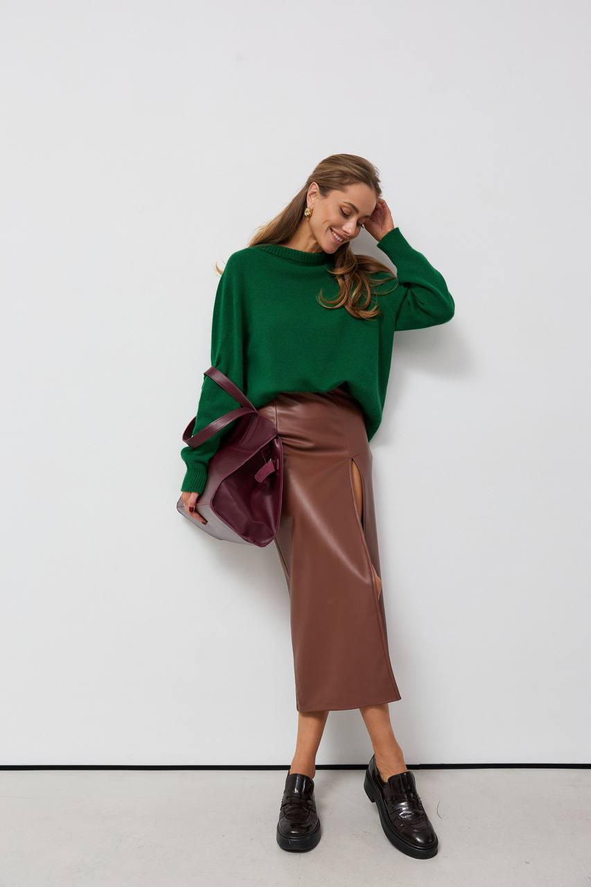 Woman wearing a green sweater and brown leather skirt against a white background