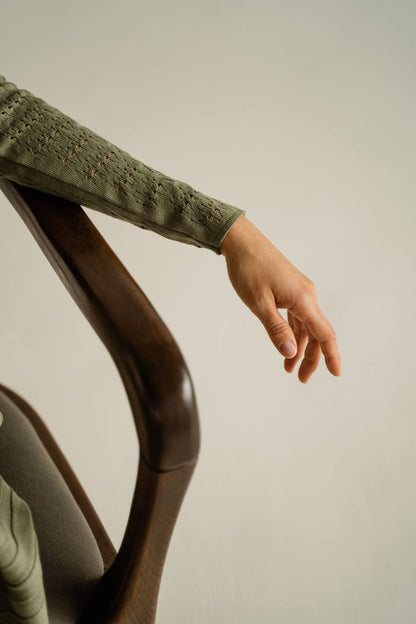 Person wearing a green sweater with lace detailing on a neutral background
