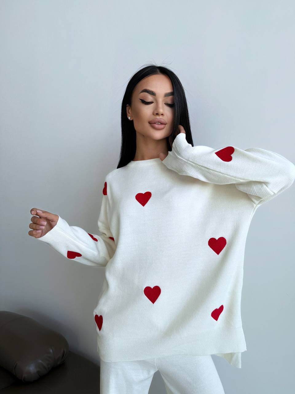 Woman wearing a white sweater with red heart patterns against a plain background
