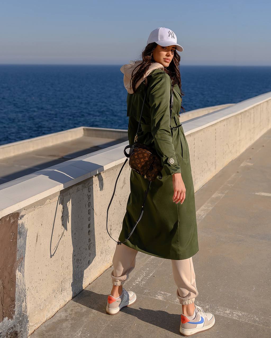 Person wearing a green coat and white cap standing by the ocean.
