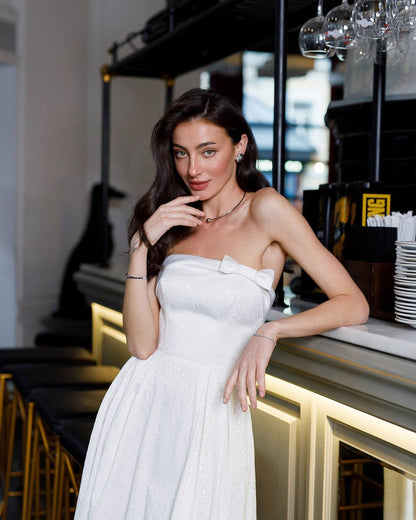 Woman in a white strapless dress standing in a modern interior setting.
