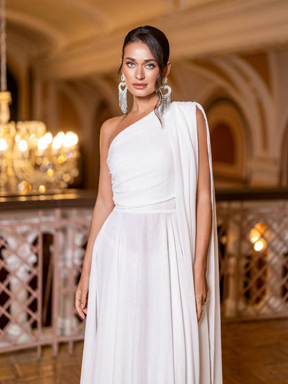 Woman in a white one-shoulder gown standing in an elegant indoor setting with chandeliers.