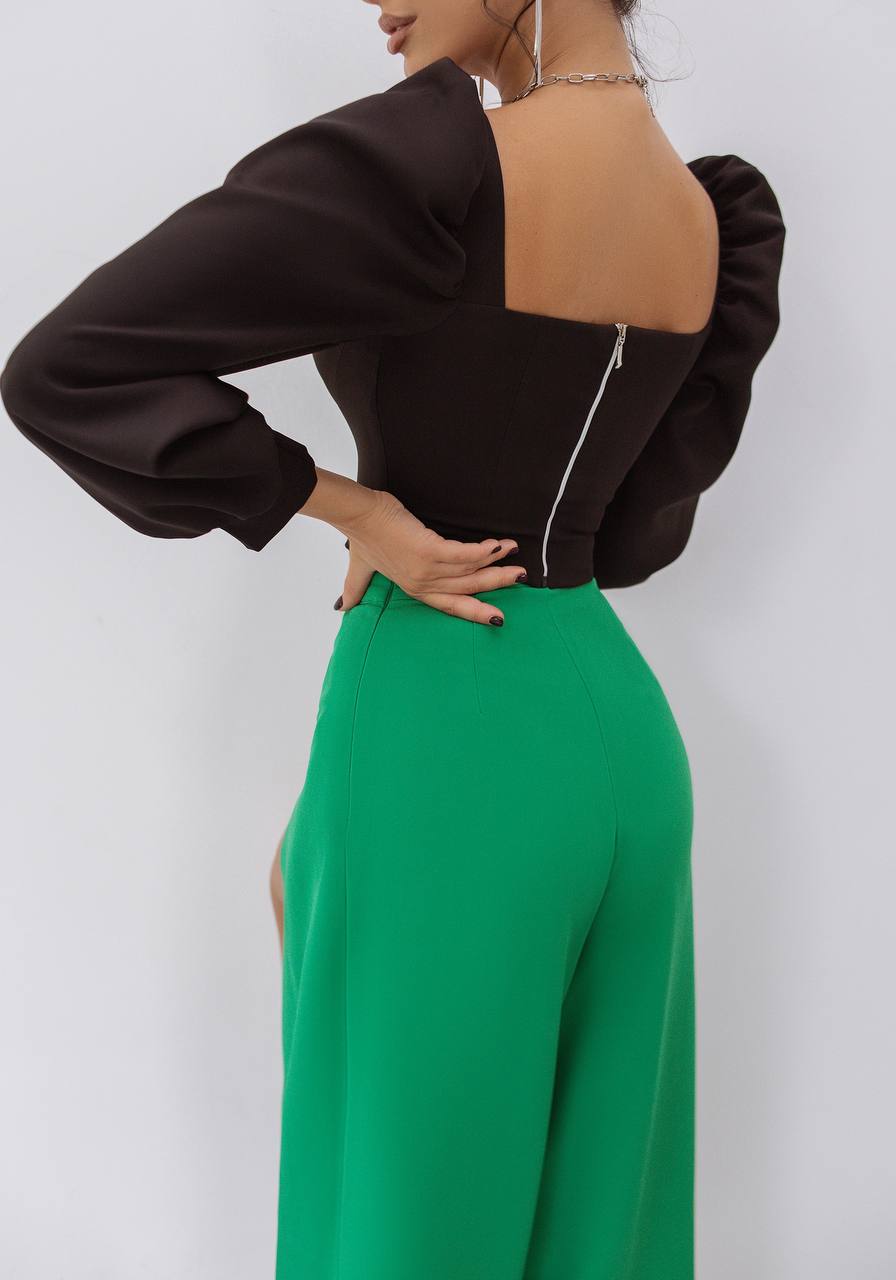 Person wearing a black open-back top and green pants on a white background