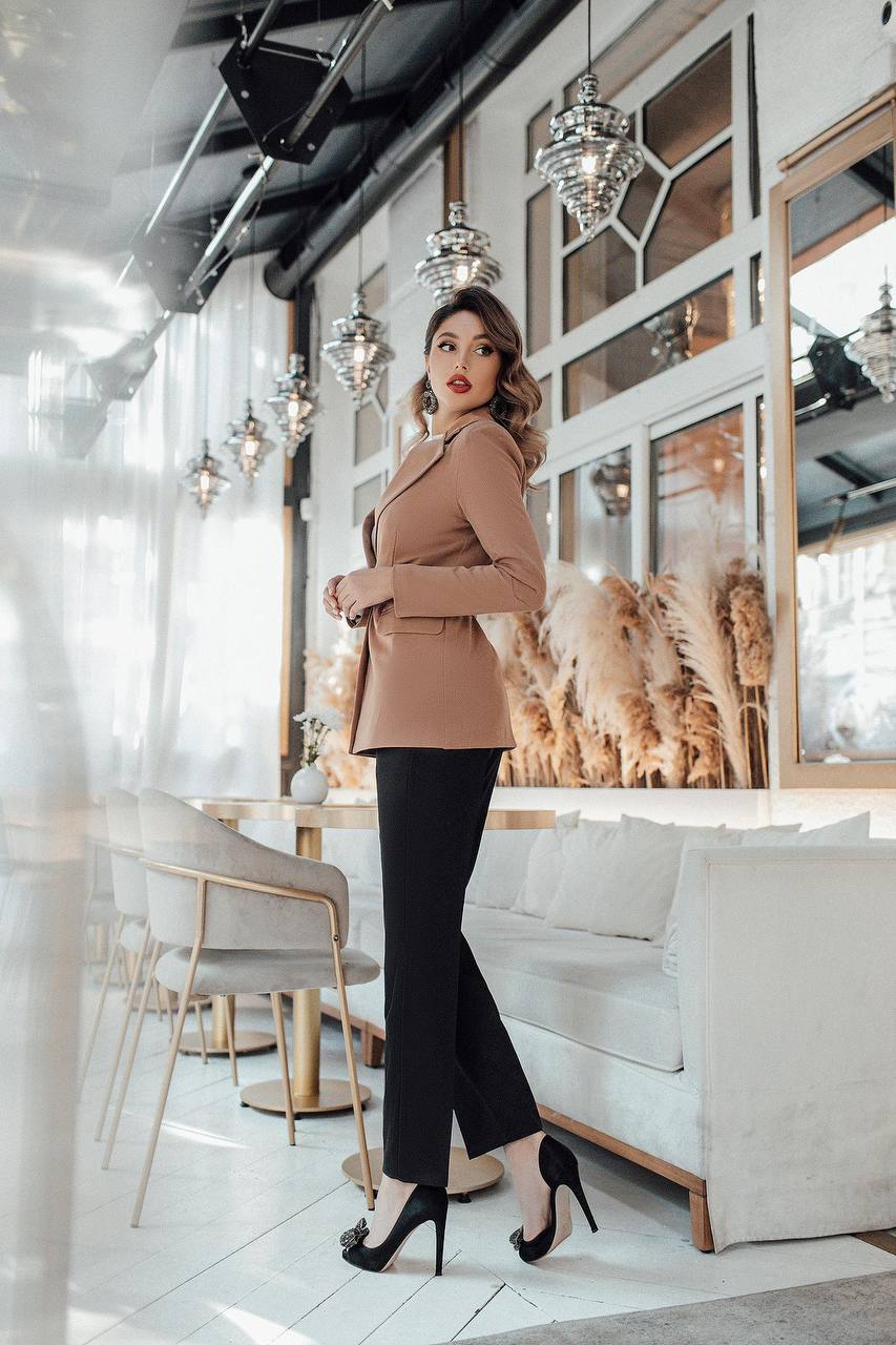 Woman in a stylish outfit standing in an elegant interior setting with mirrors and decor.