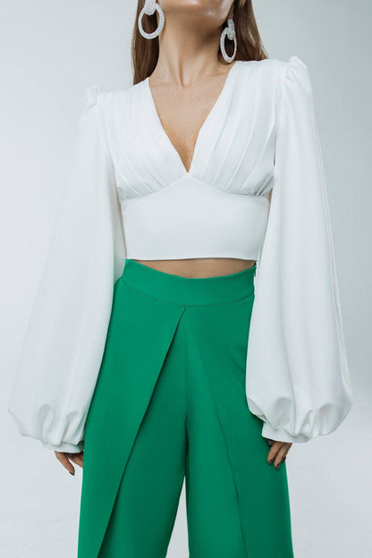 Person wearing a white blouse with long sleeves and green pants on a light gray background