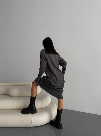 Woman in a gray dress sitting on a white curved sofa against a plain wall.