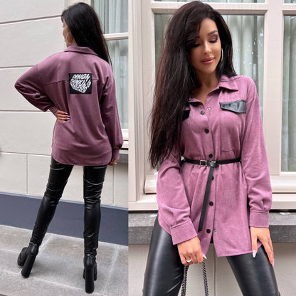 Woman wearing a purple jacket with a brand logo, standing in front of a window.