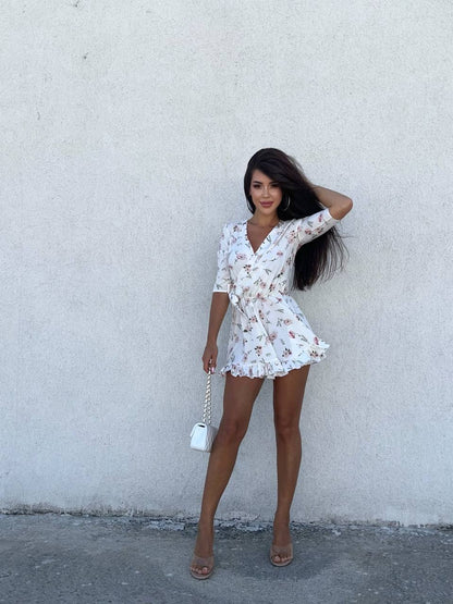 Woman in a floral dress standing against a plain wall