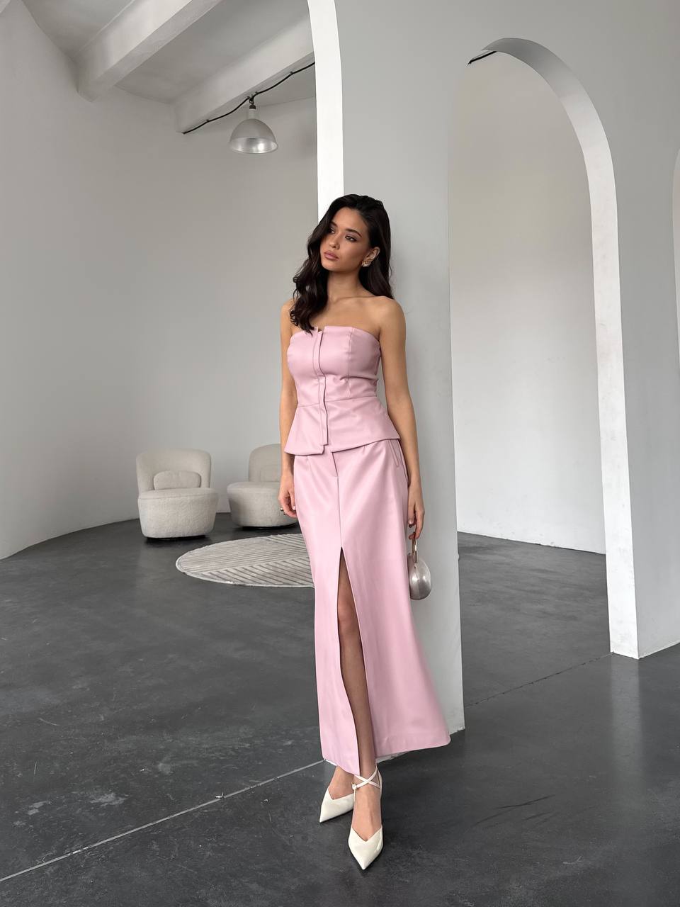 Woman in a pink strapless dress standing in a modern room with white walls and gray floor.
