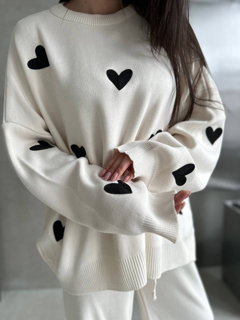 White sweater with black heart patterns worn by a person against a neutral background