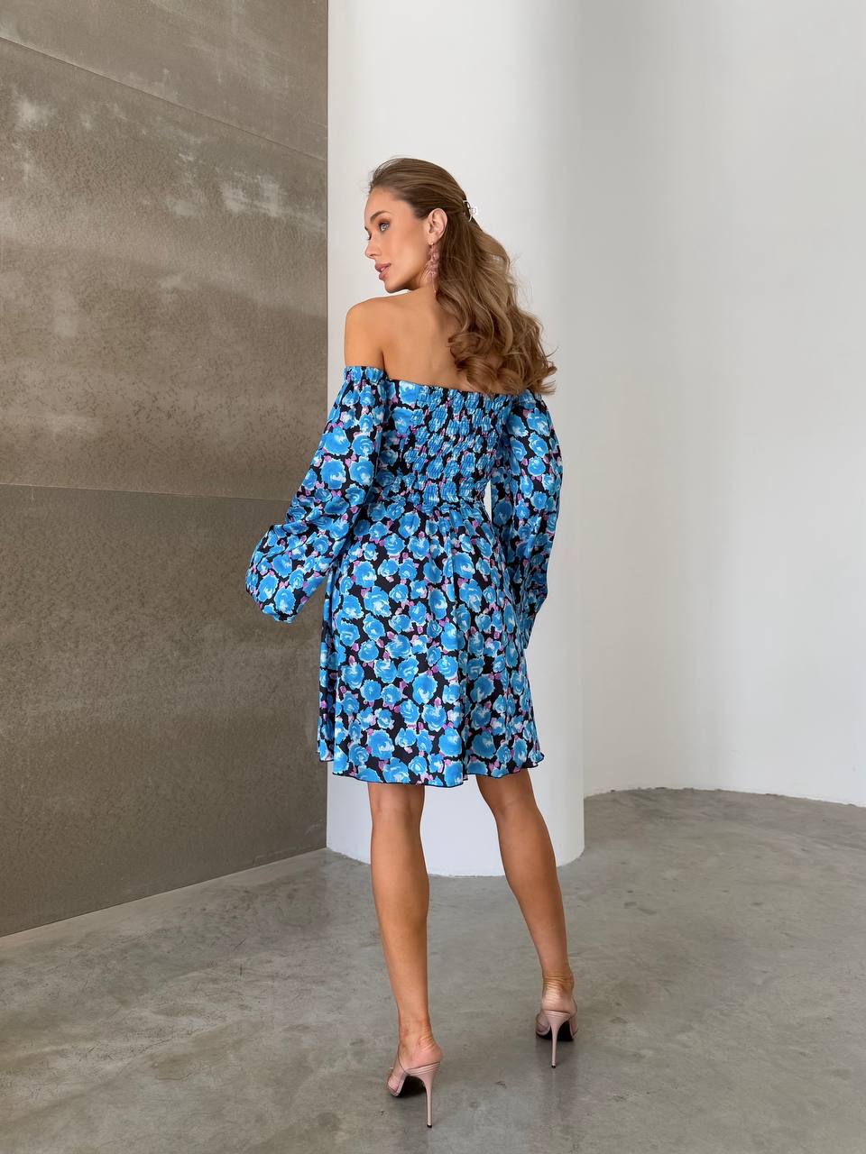 Woman wearing a blue floral off-shoulder dress against a plain wall.