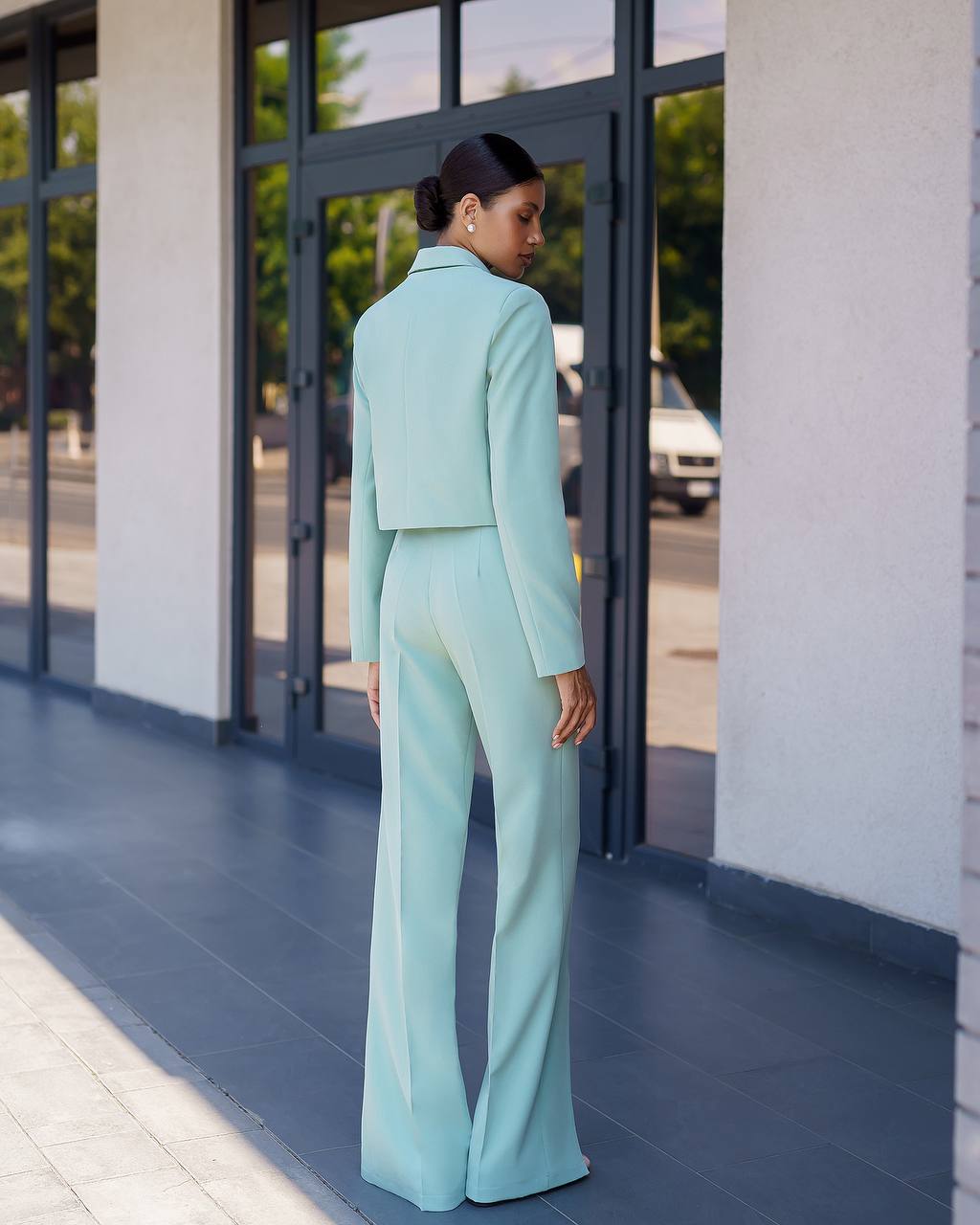 Woman in a light blue suit standing outside a building with large windows.