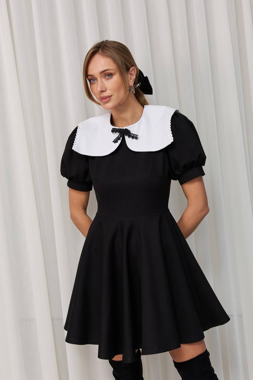 Woman wearing a black dress with a white collar against a white curtain background