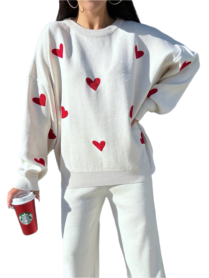 White sweater with red heart patterns worn by a person, holding a Starbucks cup.