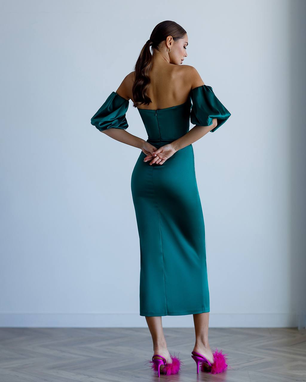 Woman wearing a teal off-shoulder dress with puffed sleeves against a plain background