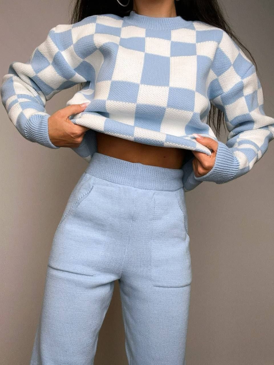 Person wearing a blue and white checkered sweater and pants against a neutral background